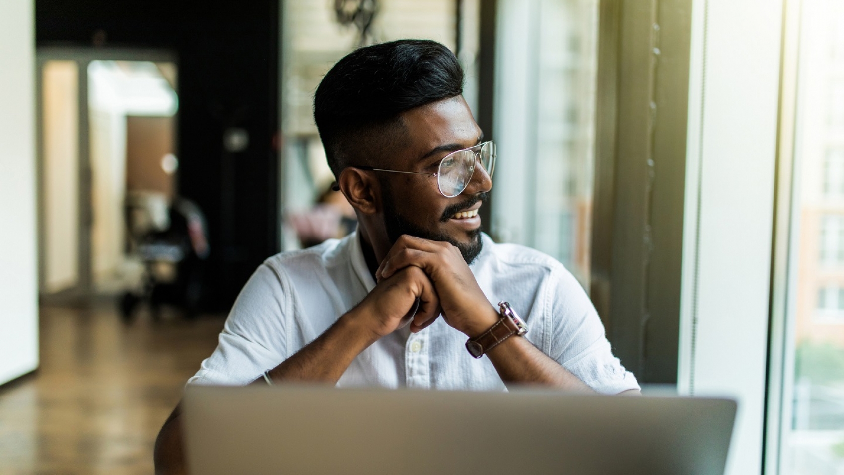 Man with glasses sat at a laptop looking out of a window